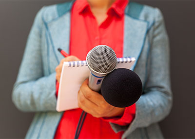 A person writes on a notepad while holding two microphones.