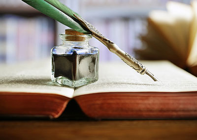Quill pen resting against a bottle of ink on top of a book