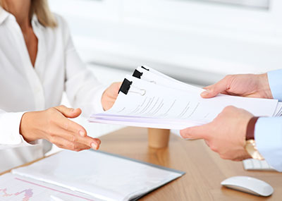 A person hands binder clipped reports to another person