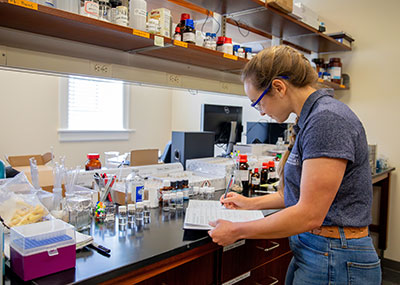 A student writes in a book while surrounded by various lab equipment