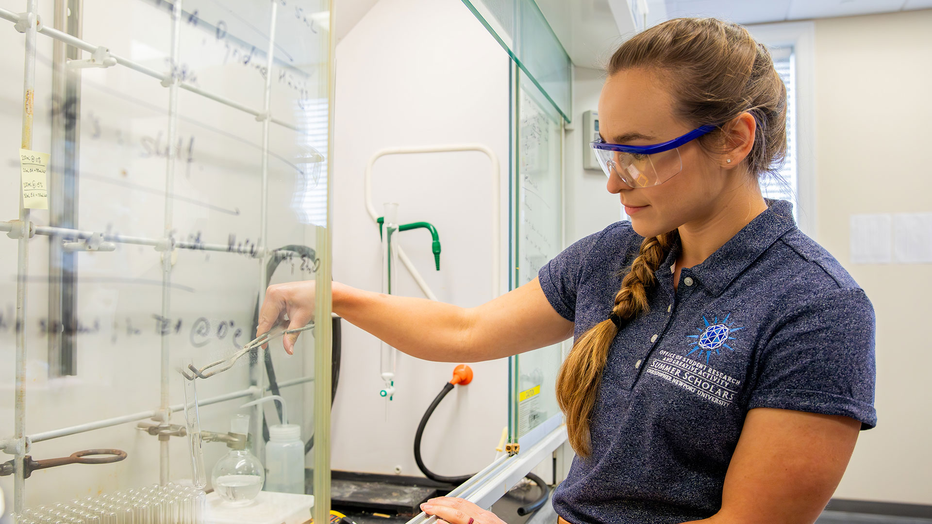 Student in a chemistry lab holding a beaker with tongs