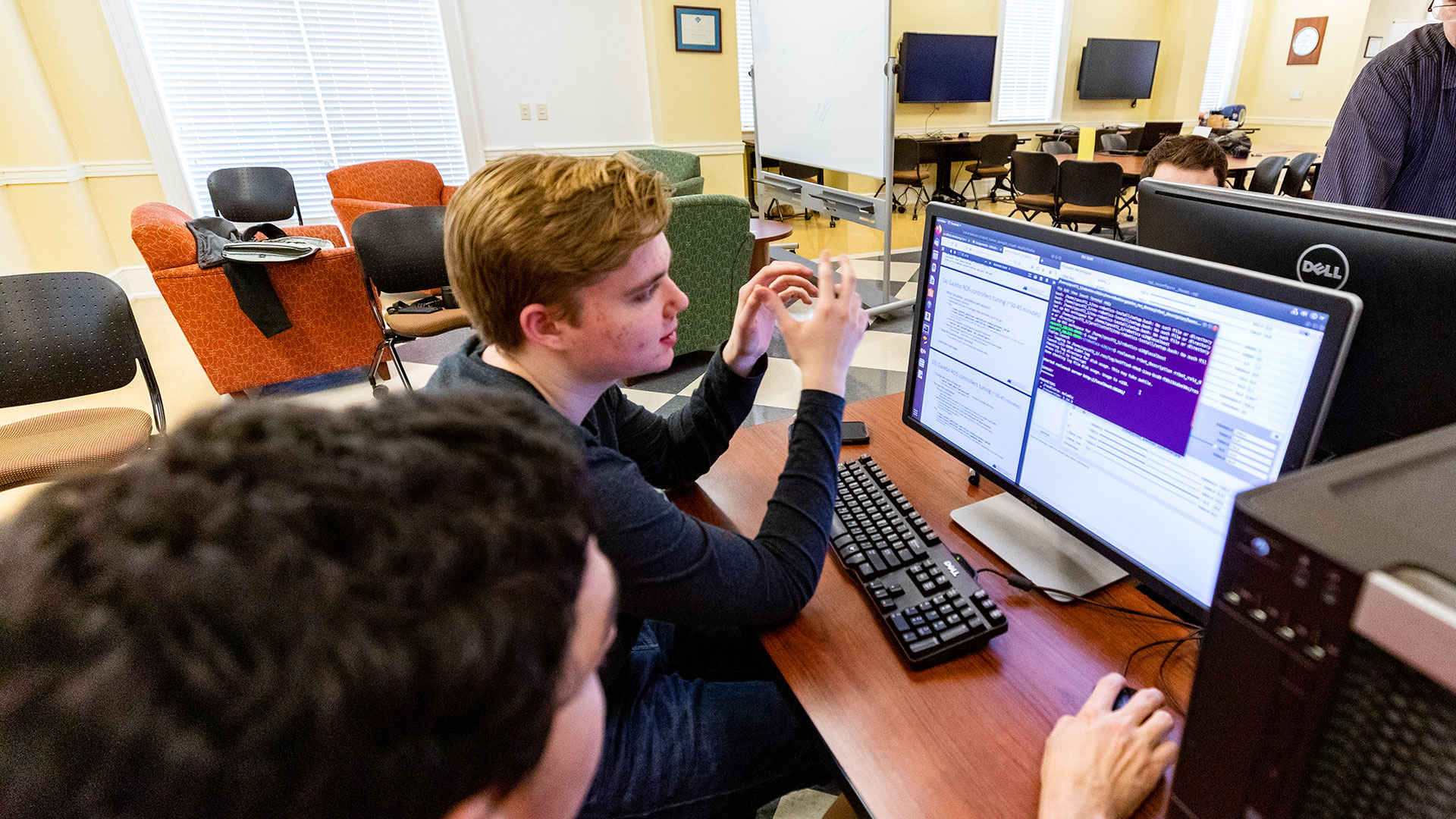 Students in a computer lab sitting at a computer with code on it