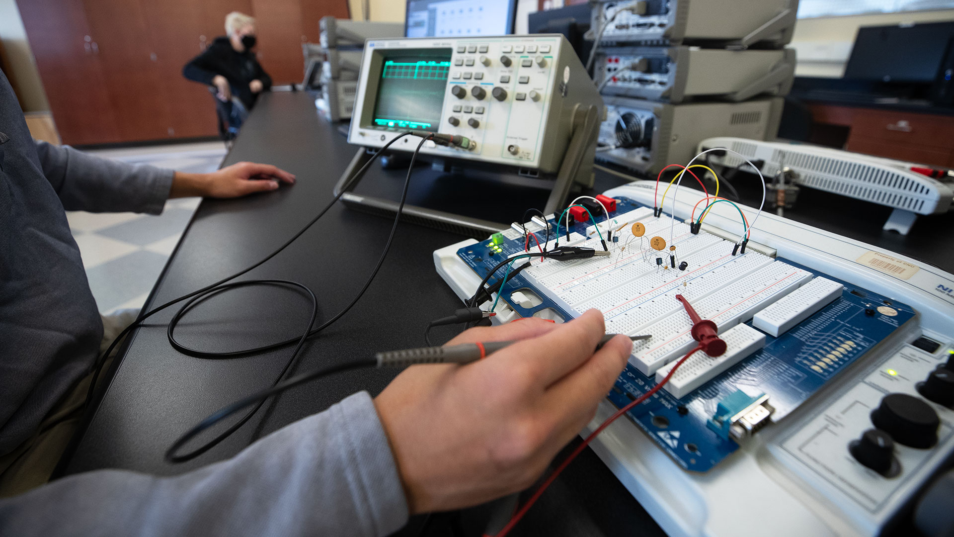 Close-up of a student working on a bread board with soldering iron and electronics meter