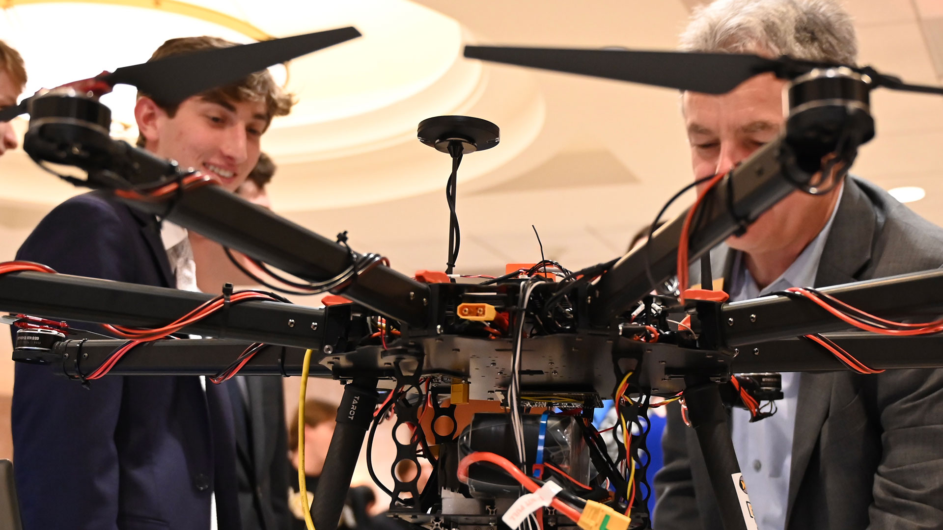 A drone stands in the foreground while a student and professor look on in the background