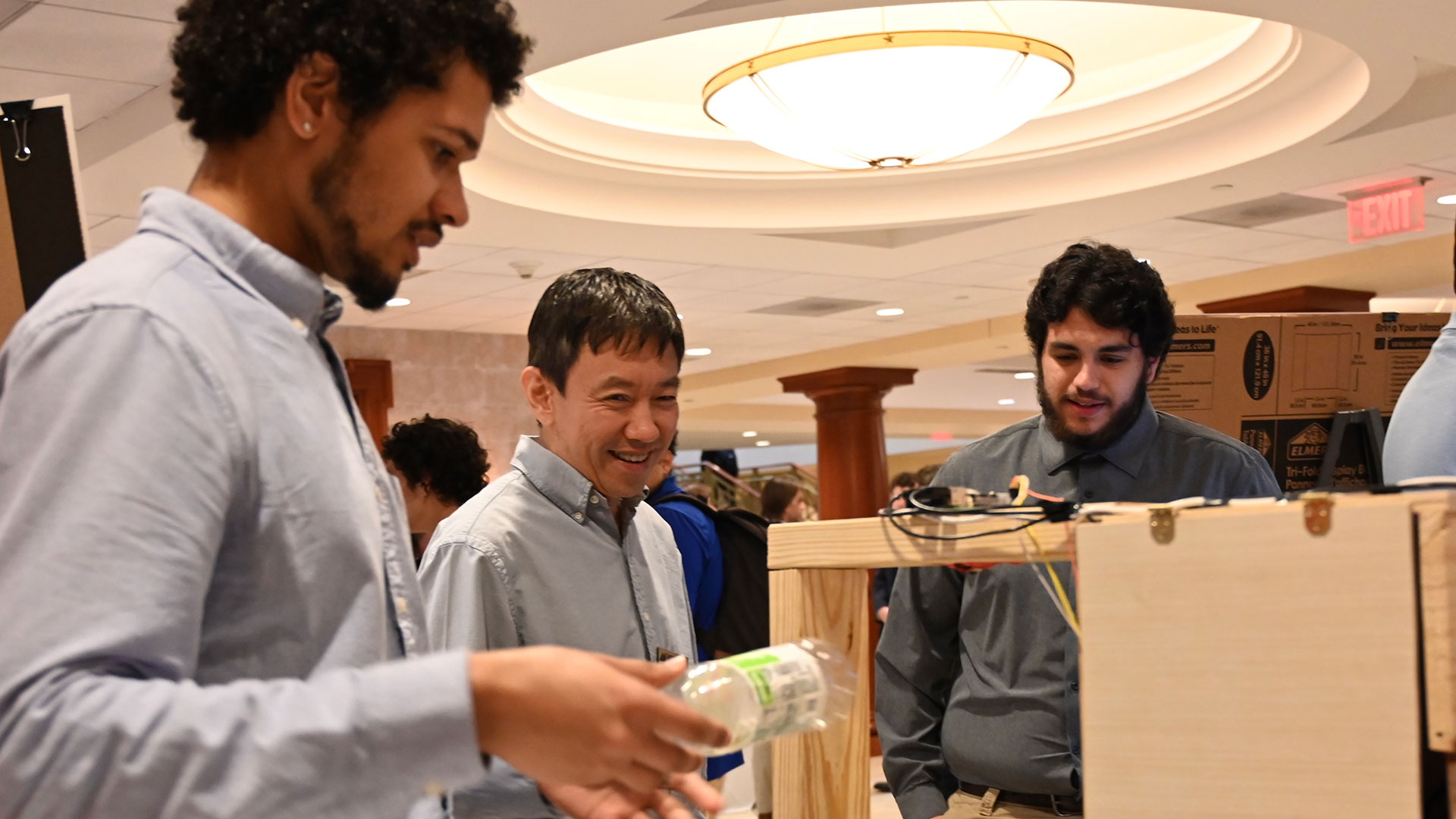 Two SEC students and a professor look at a machine built