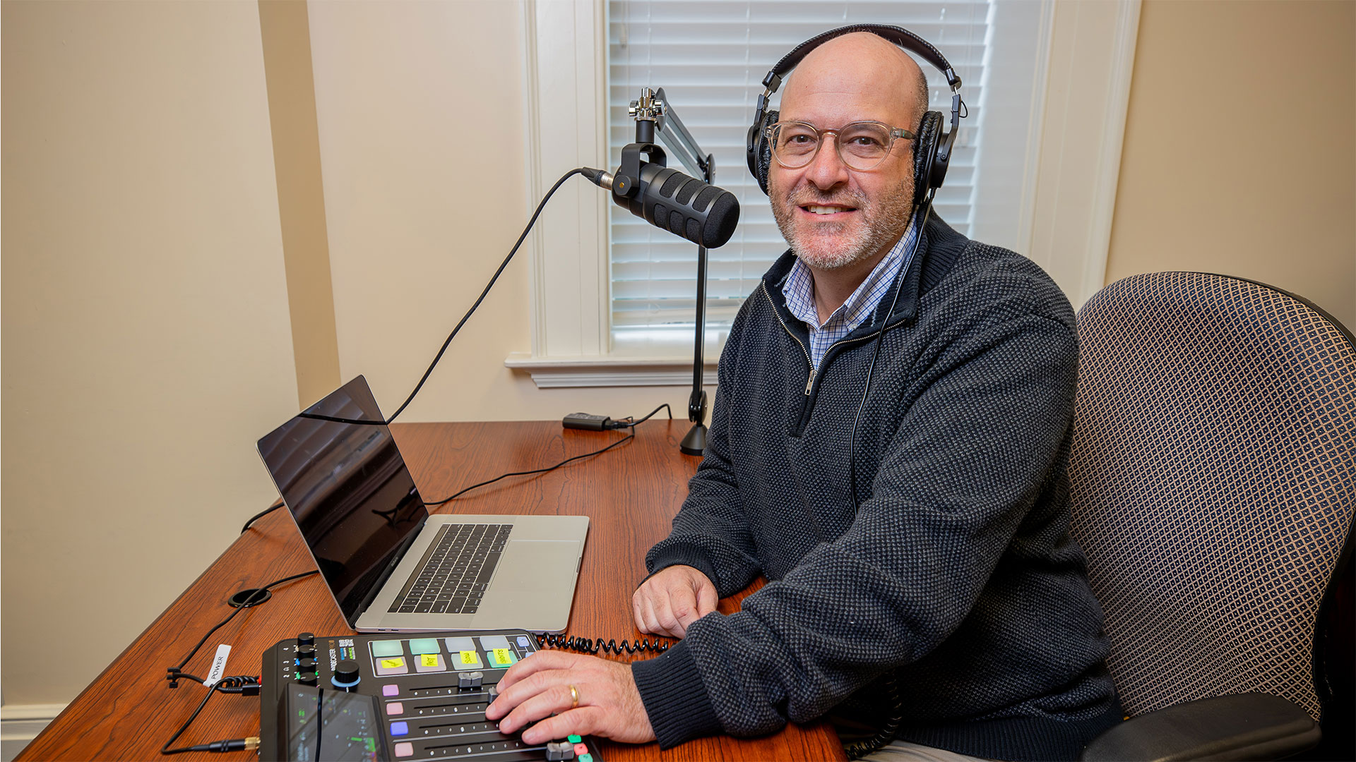 Andrew Falk looks at a camera while having his podcasting equipment on display on his desk