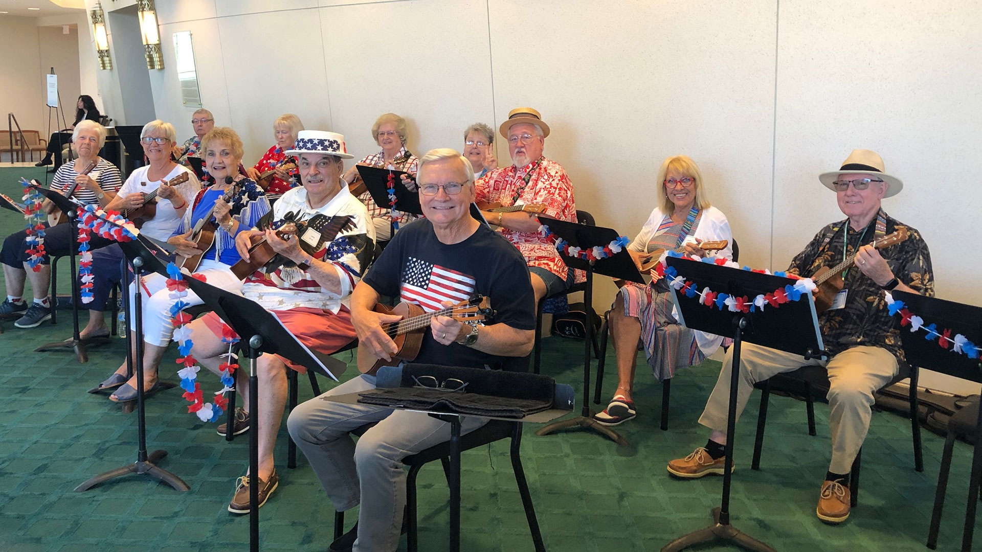A group of Lifelong Learning Society members sit with ukuleles in an atrium.