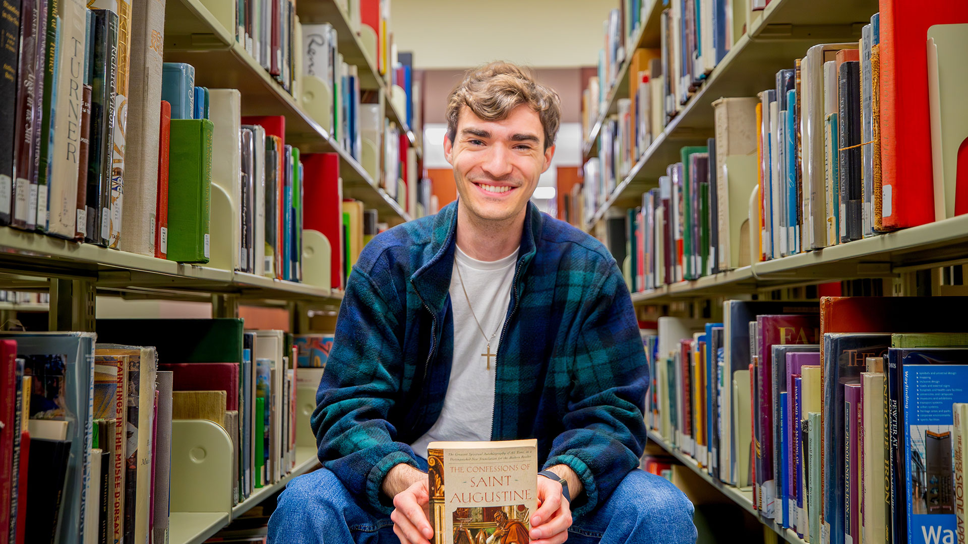 Philosophy student holding a book about St. Augustine sitting in a library