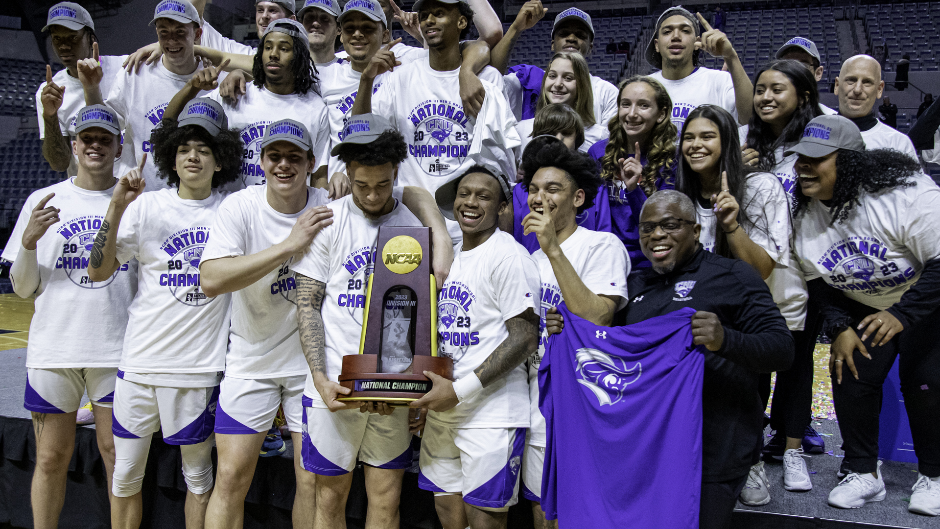 The 2023 Christopher Newport University Men's Basketball team celebrate with their national championship trophy.