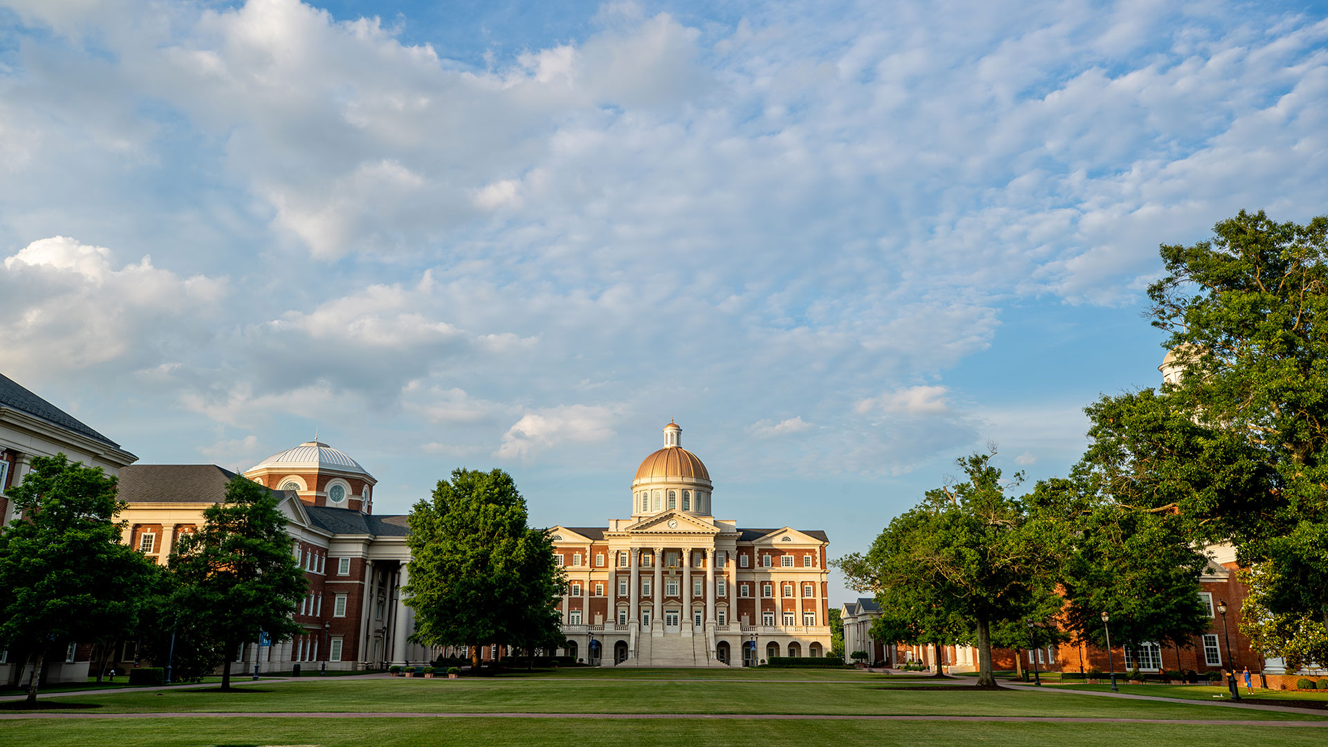 Christopher Newport Hall from the far end of the Great Lawn as the sun begins to set. Blue sky filled with clouds 