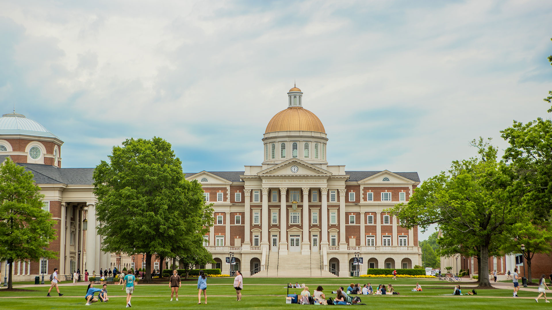 Christopher Newport Hall looms large as students sit on the Great Lawn
