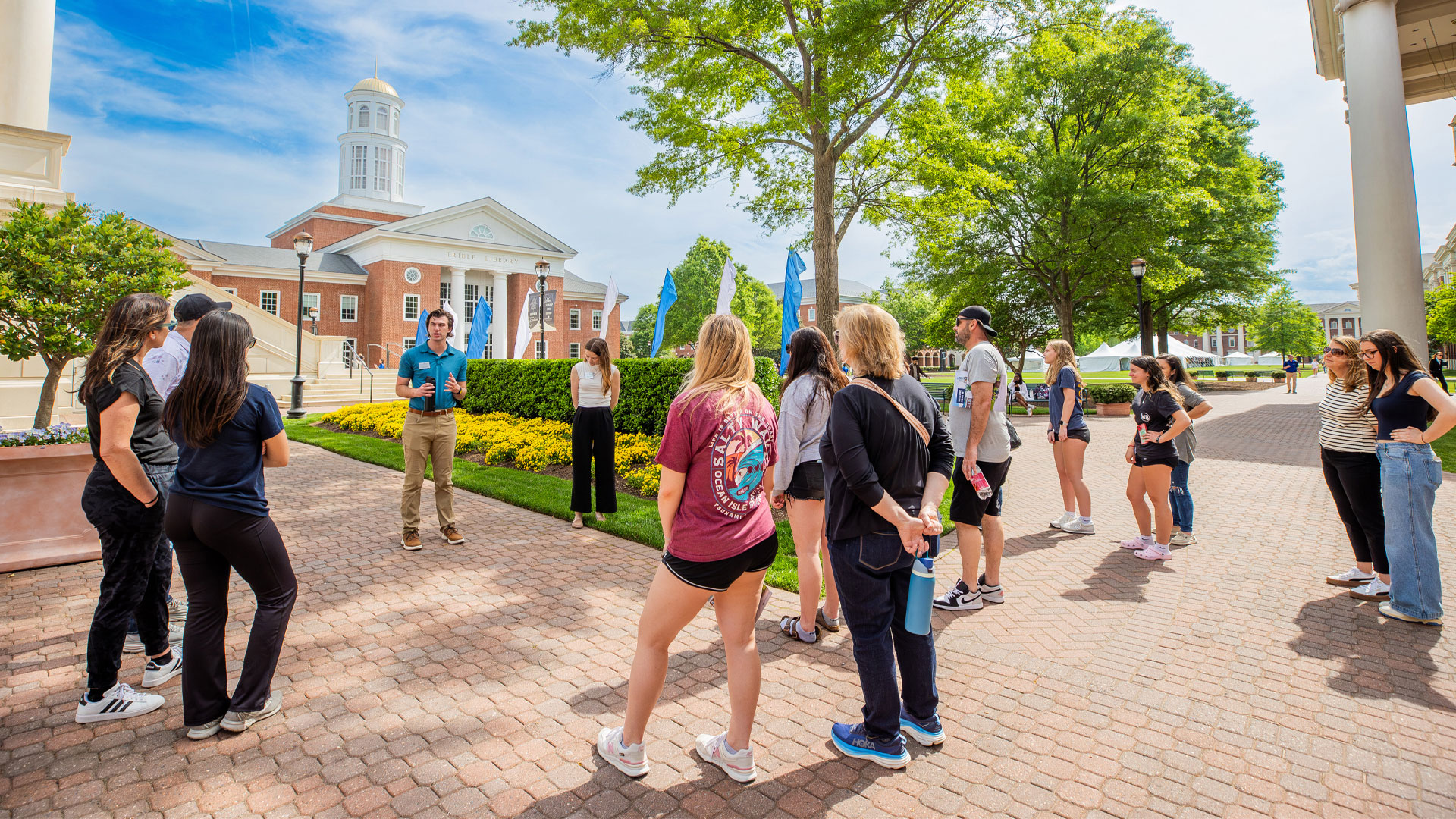 A student ambassador in a blue polo, center, talks with prospective students while giving a tour to them and their families 