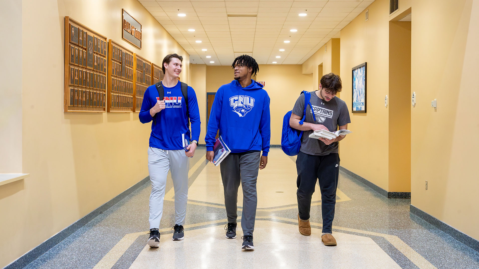 Three students in CNU Captains athletic gear walk down the hall in Freeman