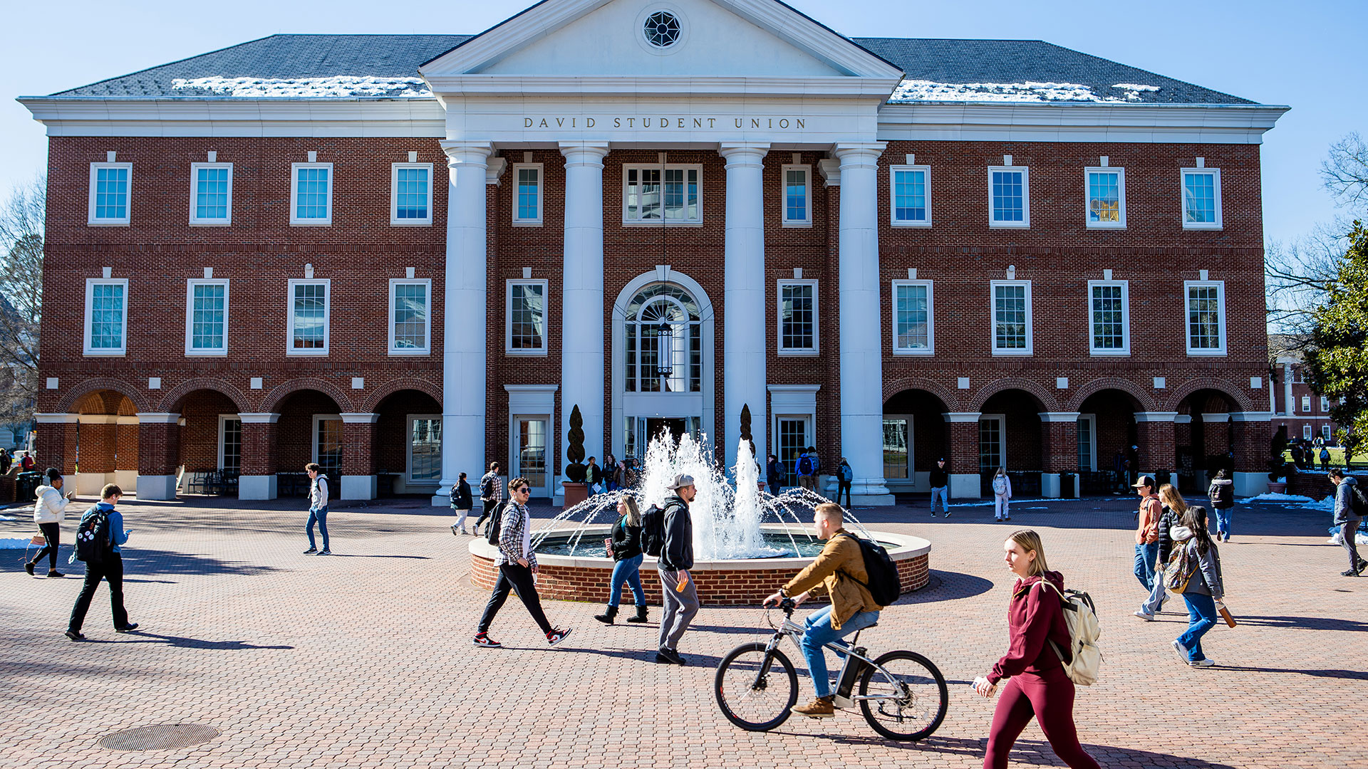 Students walk and bike in front of a fountain and the David Student Union