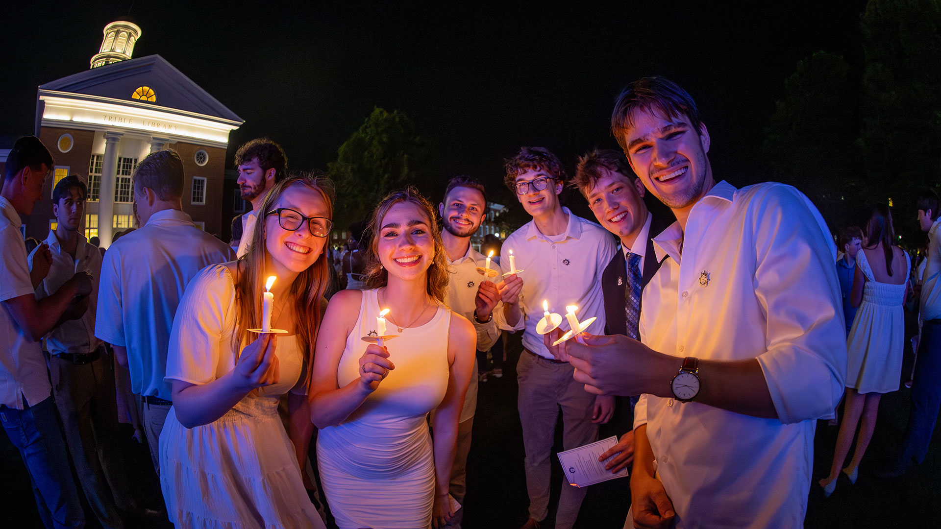 Students wearing white and holding lit candles