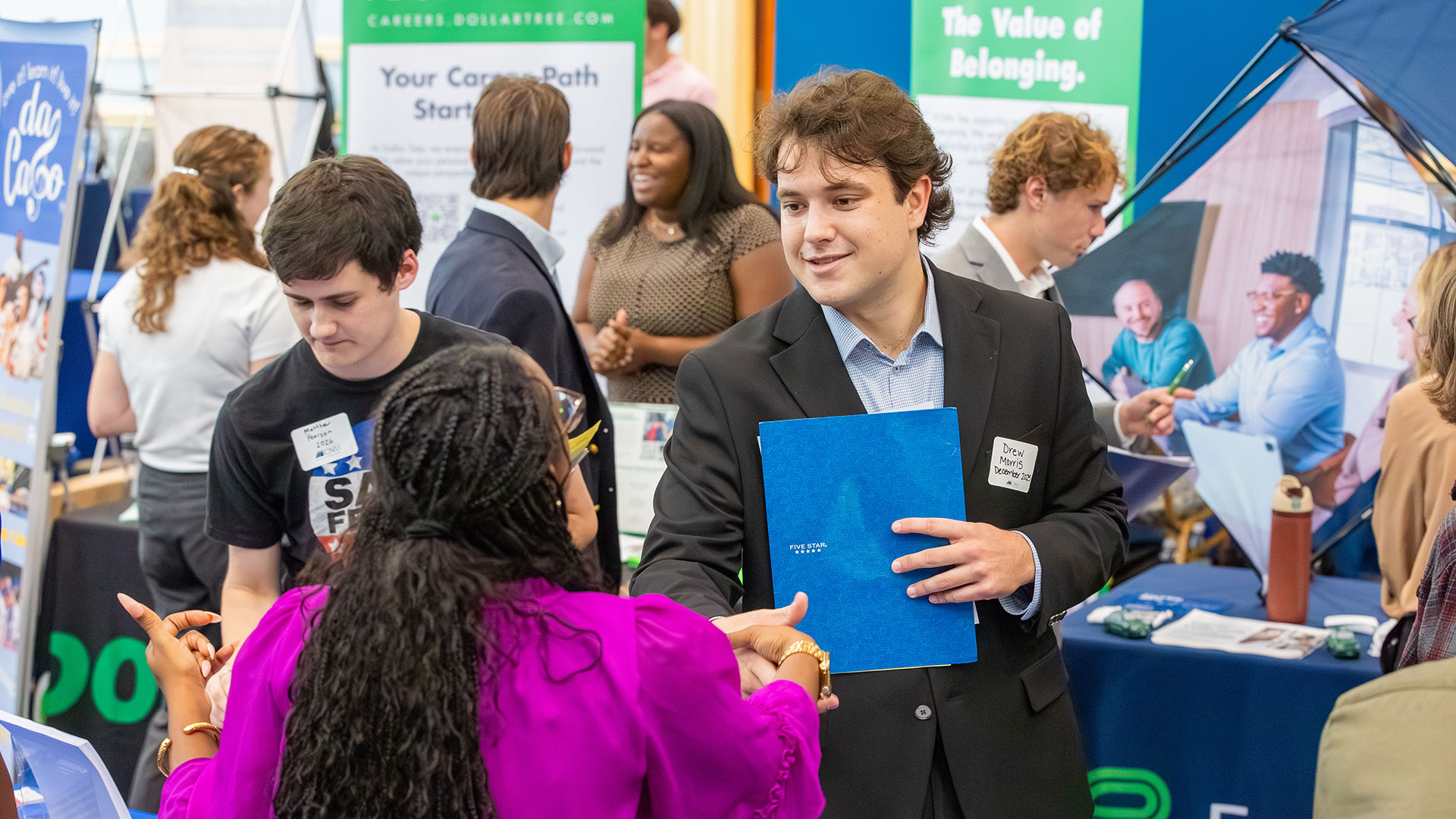 A student in a suit shakes hands with an individual during a career and internship fair.