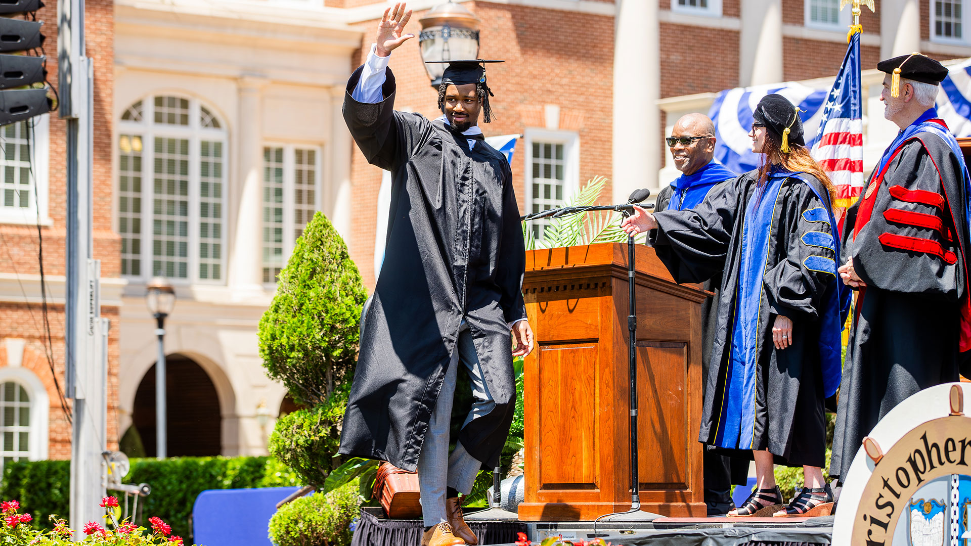 A student in a black cap and gown walks across the stage.