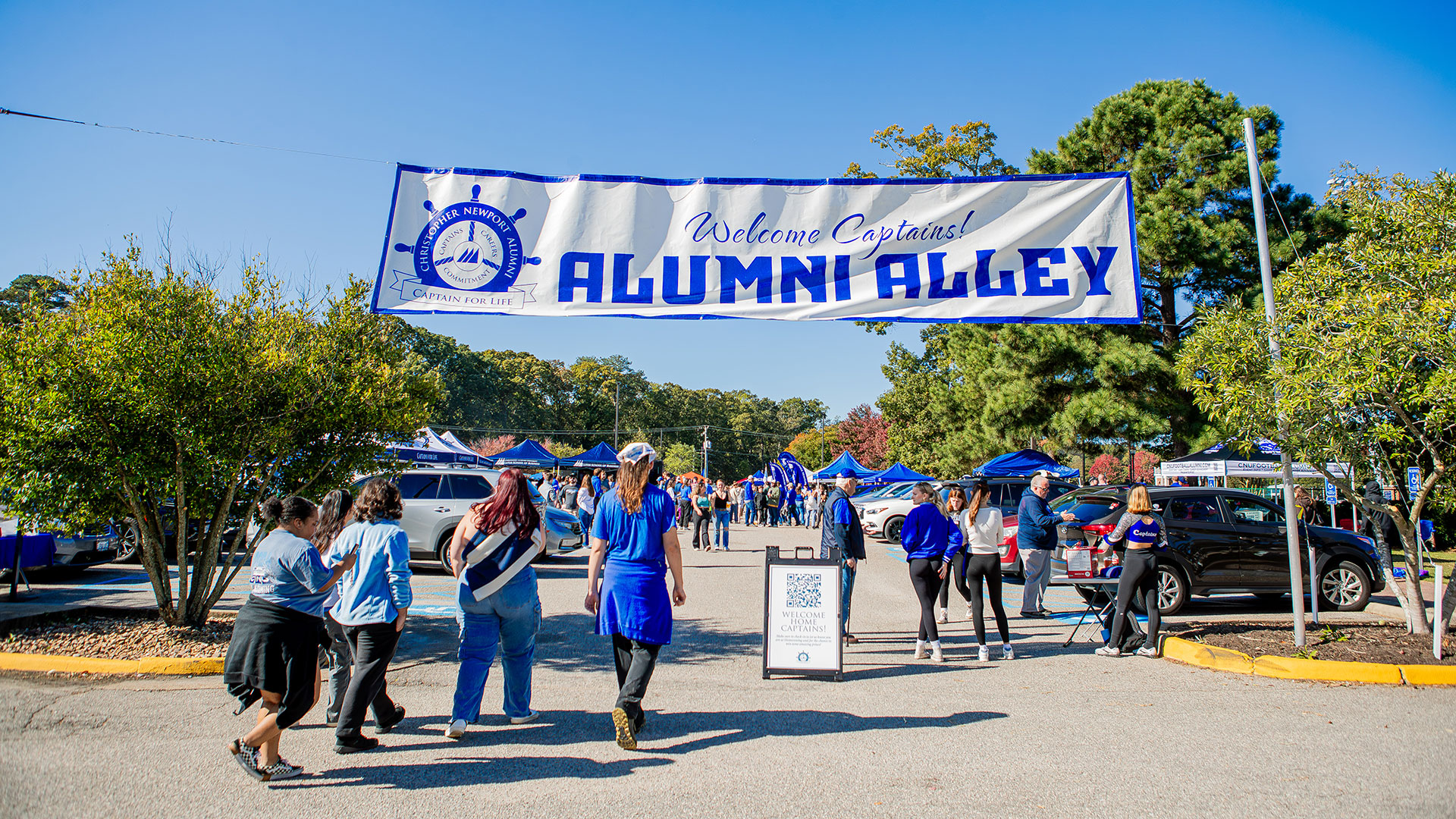 People walk into a tailgate lot with a banner that reads Welcome Captains! Alumni Alley