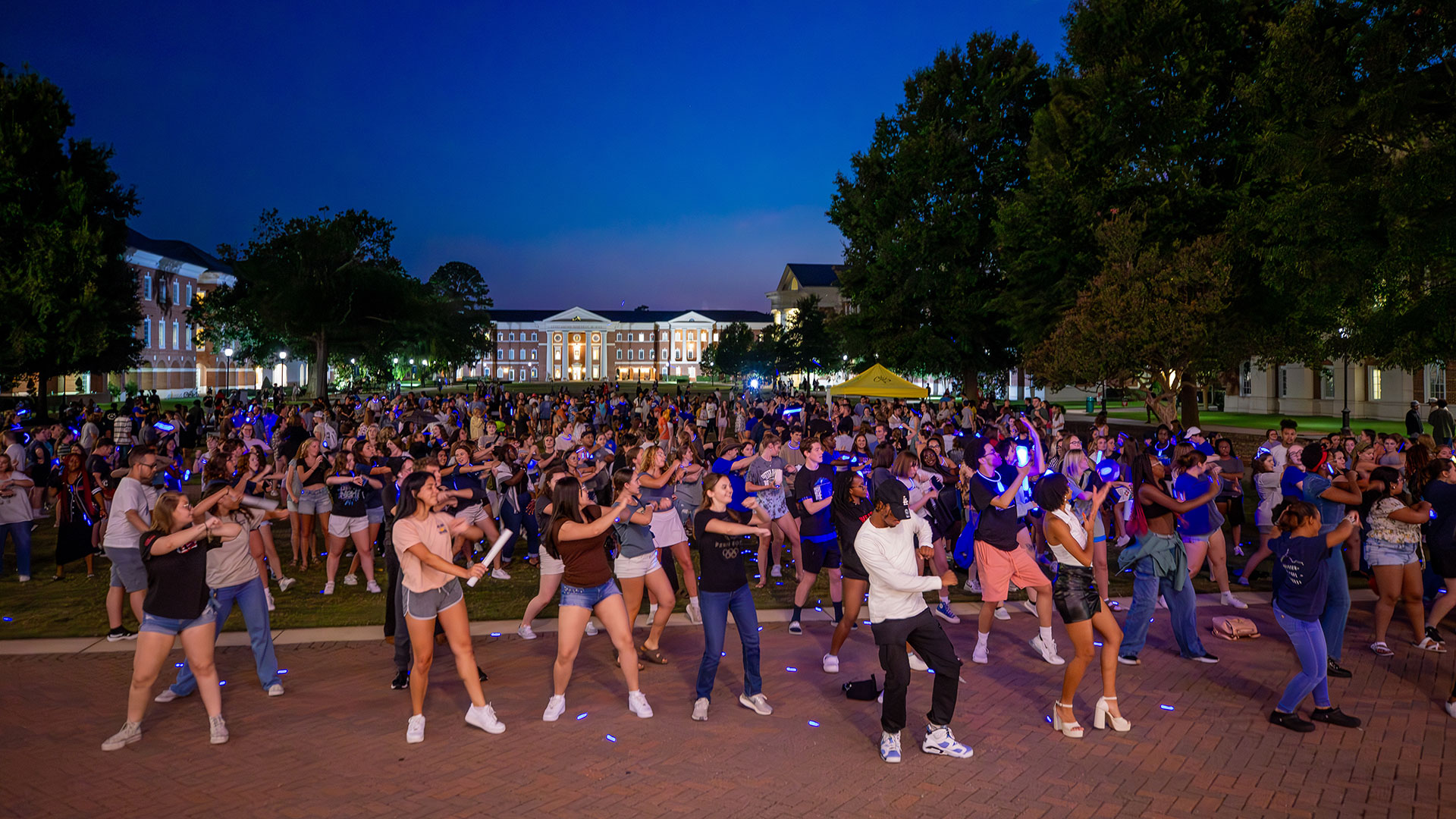 A large group of students Dance on the Great Lawn at dusk.