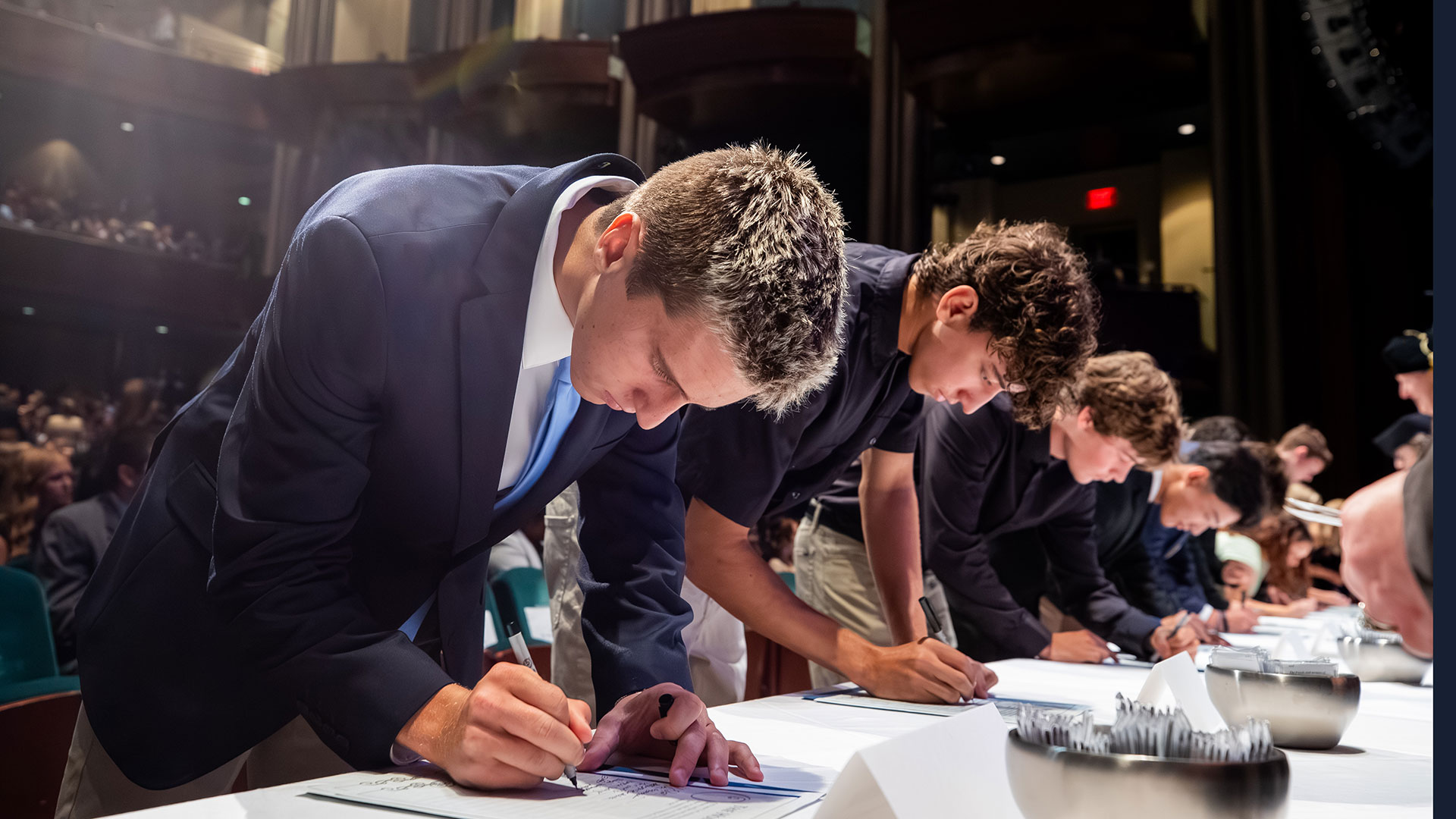 A student in a suit and tie leans over a table to sign the Honor Code at Christopher Newport University