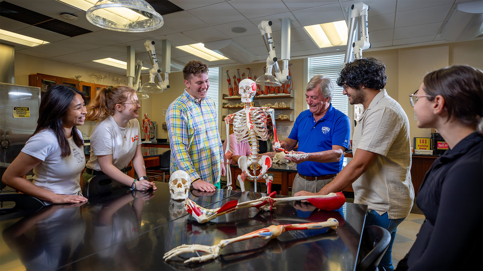 Students gather beside a professor who shows them a skeletal muscular model