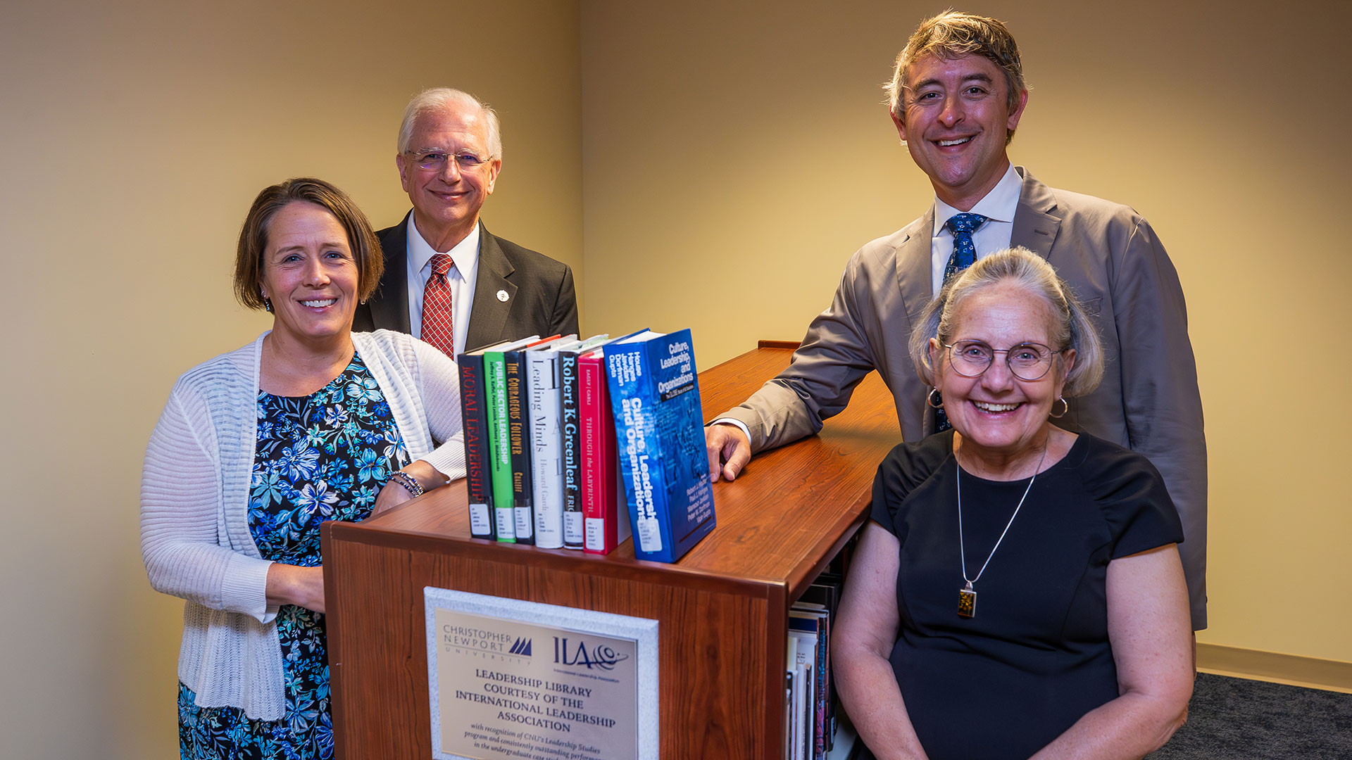 Four individuals stand around a short bookshelf housing a donated leadership learning library from the ILA.