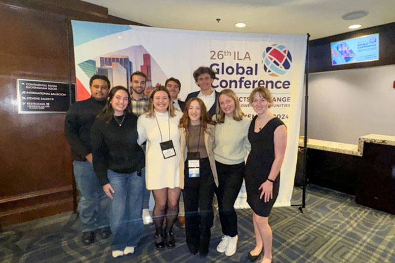 PLP team standing in front of an ILA conference banner