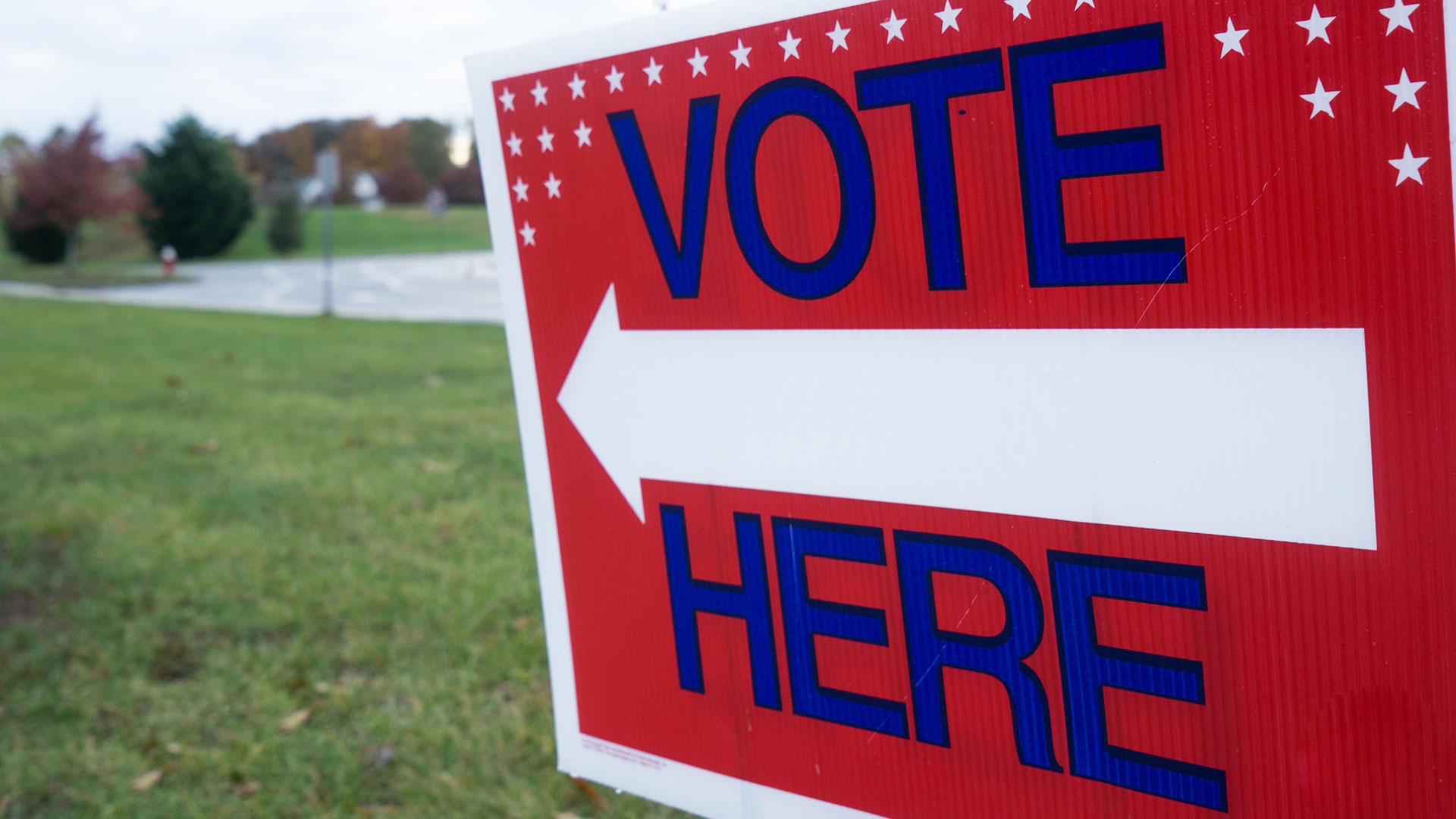 A red sign with Vote Here in blue along with a blue arrow pointing to the left.