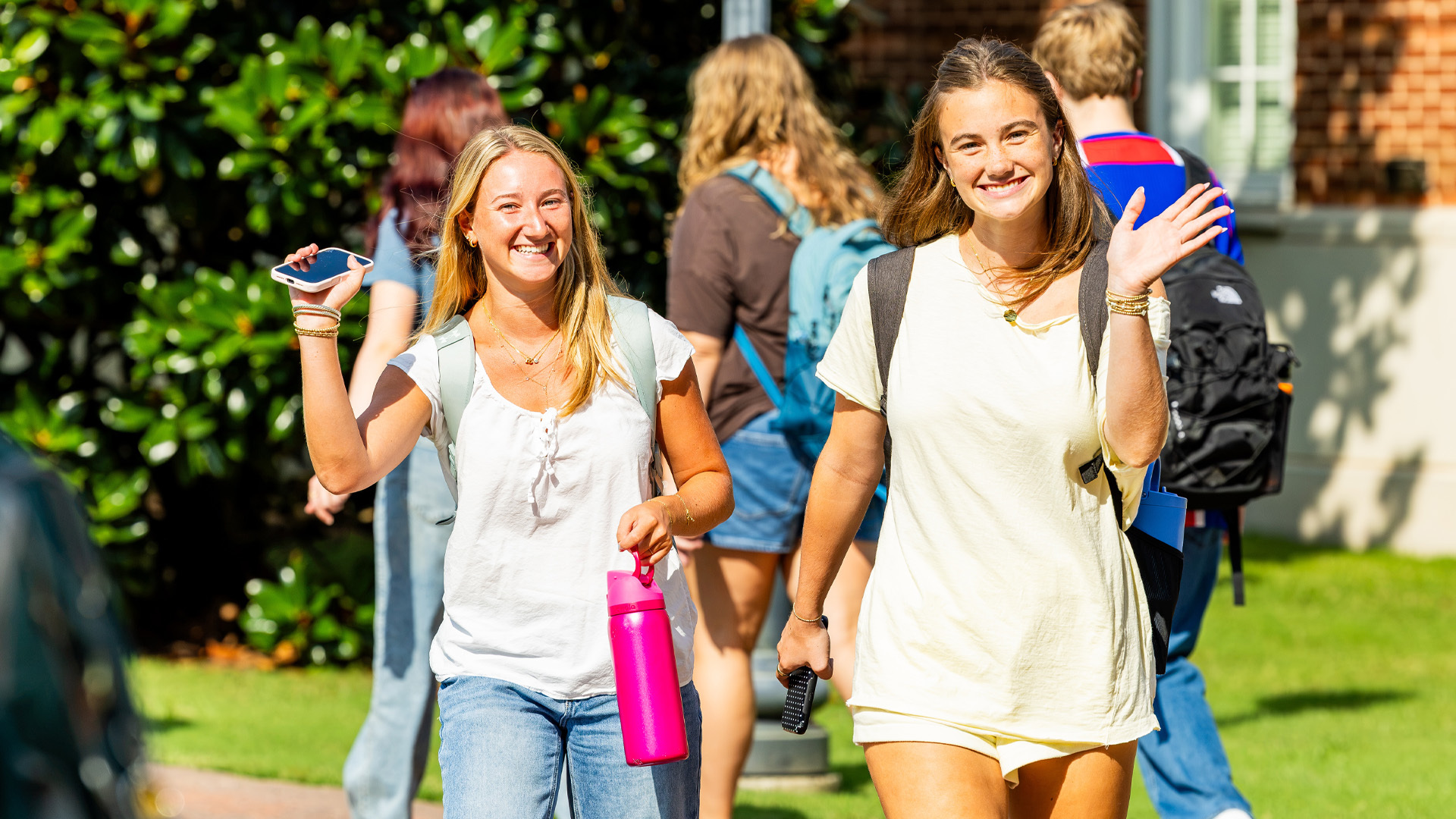 Two female students wave while walking to class.