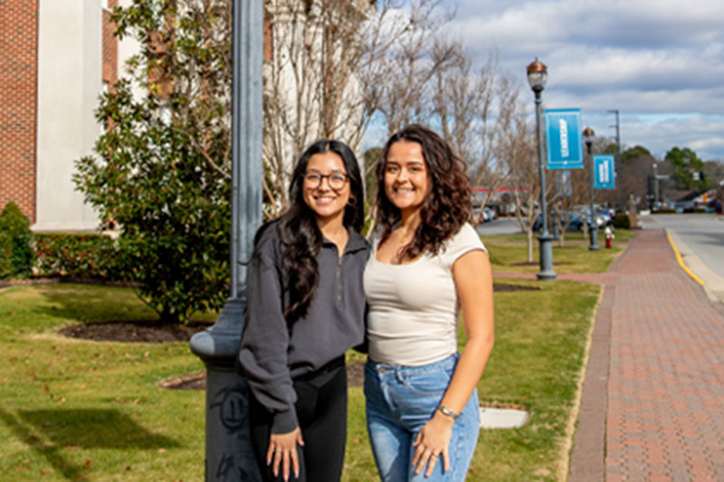 Alexandra Delgado and Niurka Verduzco Rios standing beside a light pole with a banner that says Service