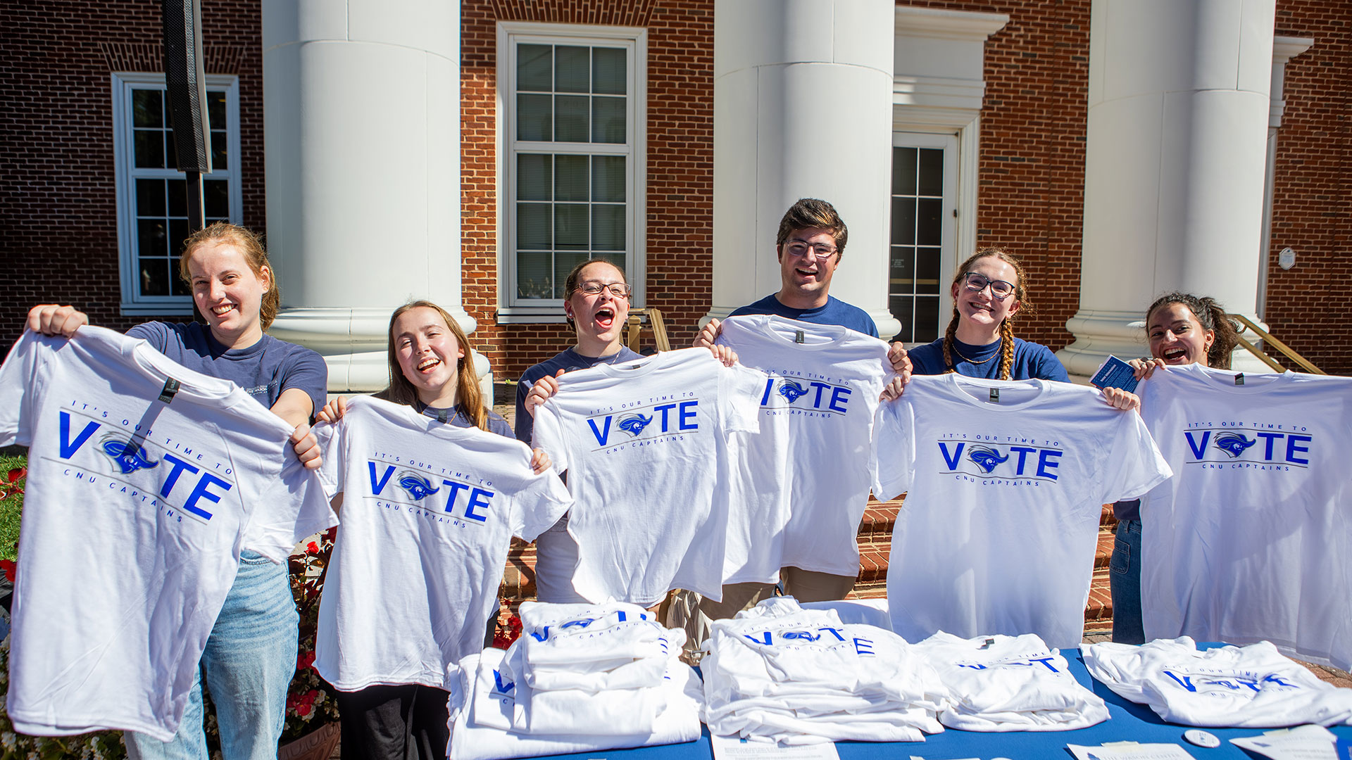 Students smiling and holding up Captains Vote t-shirts