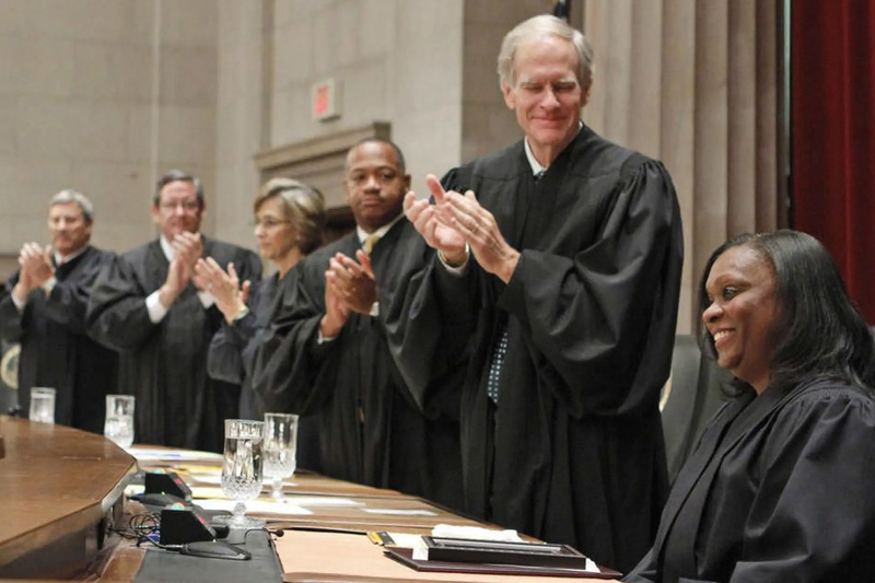 Virginia Supreme Court Justice Cleo Powell sits in the foreground while being applauded by her fellow Justices.