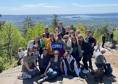 A group stands on a high point overlooking a verdant landscape holding a CNU flag
