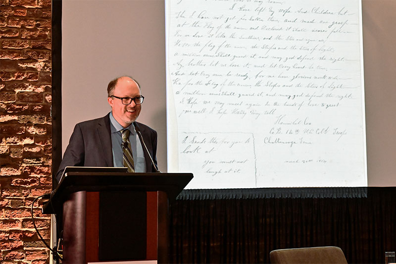 Professor Jonathan White stands at a podium with a letter projected off to his left.
