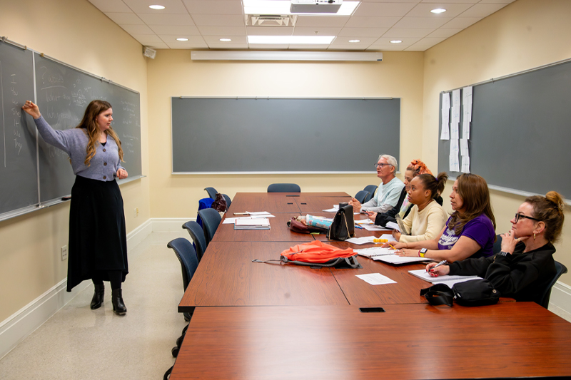 An individual stands at a chalkboard across from students learning English as a second language.