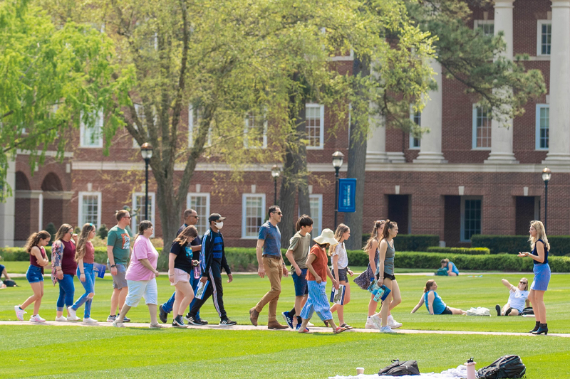 A group of prospective students and their parents follow a tour guide across the great lawn.