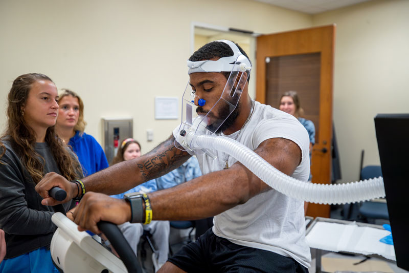 A man on an exercise with a breathing apparatus on surrounded by students