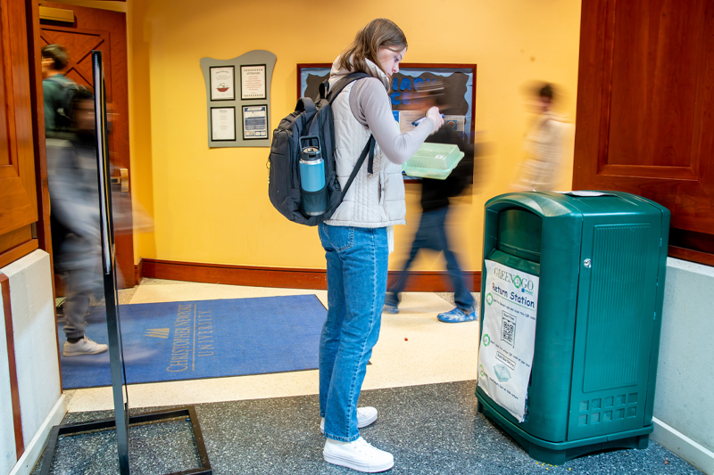 A student in focus works to return their Green2Go container while students walk around them.