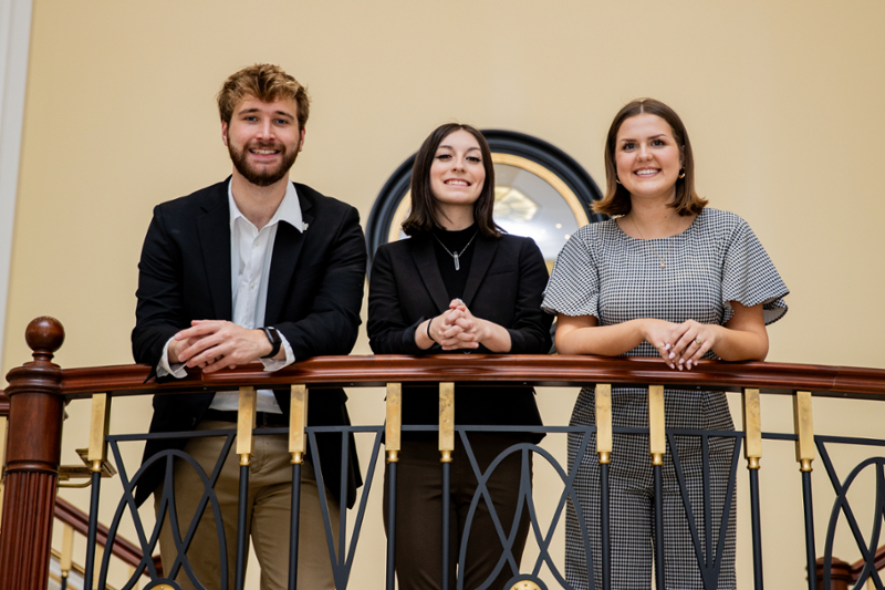 Three students lean over a railing.