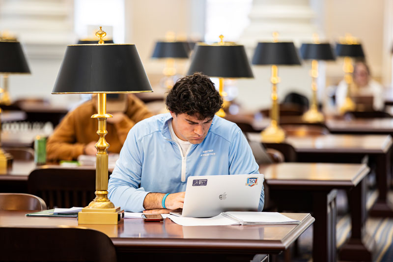 A student stares intently at their laptop while in the library.