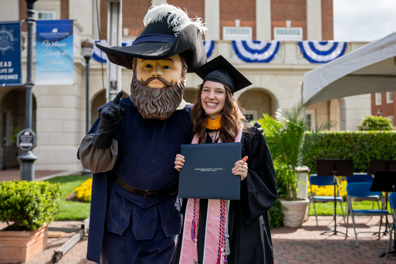 Captain Chris stands besides a graduate who is proudly showing off their diploma.