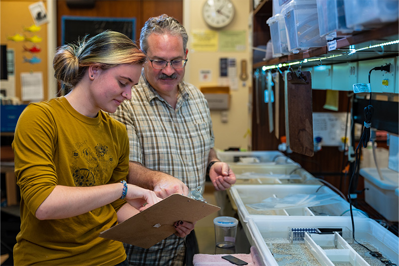 A student and professor stand in a research lab.