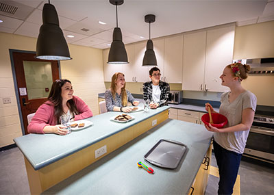 Students sit in a kitchen and talk.