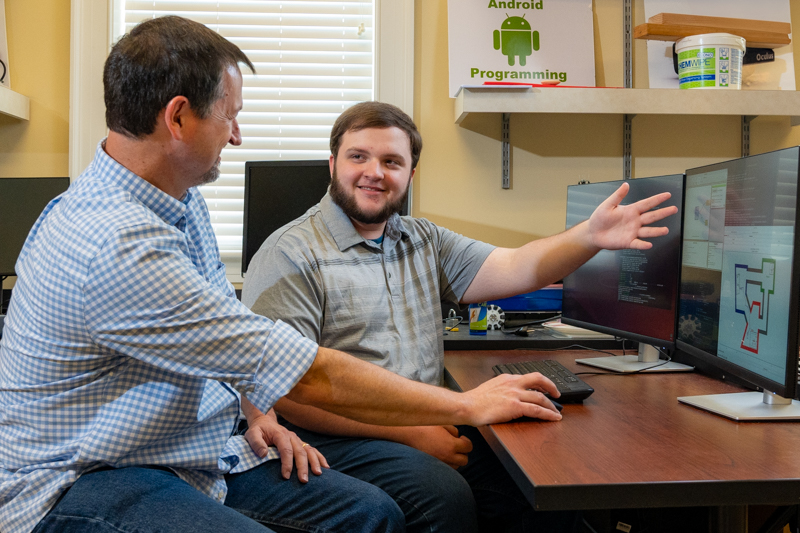 A student points at a computer screen as a professor looks on.