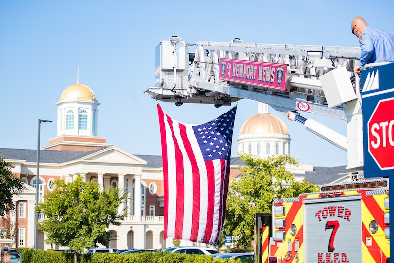 An American flag hangs from the the ladder of a Newport News Fire Department truck. The Trible Library sits in the background.