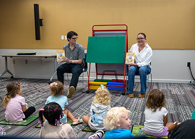 Two students sitting with an easel between them holding books, one in English and one in Spanish.