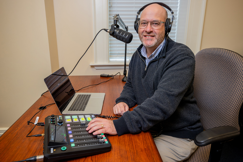 Man sitting at a microphone with headphones on recording a podcast