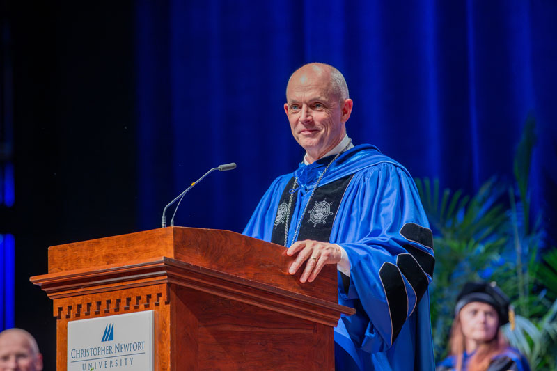 President Kelly in graduation regalia stands at a lectern