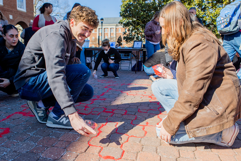 students pouring red sand in the cracks as an installation