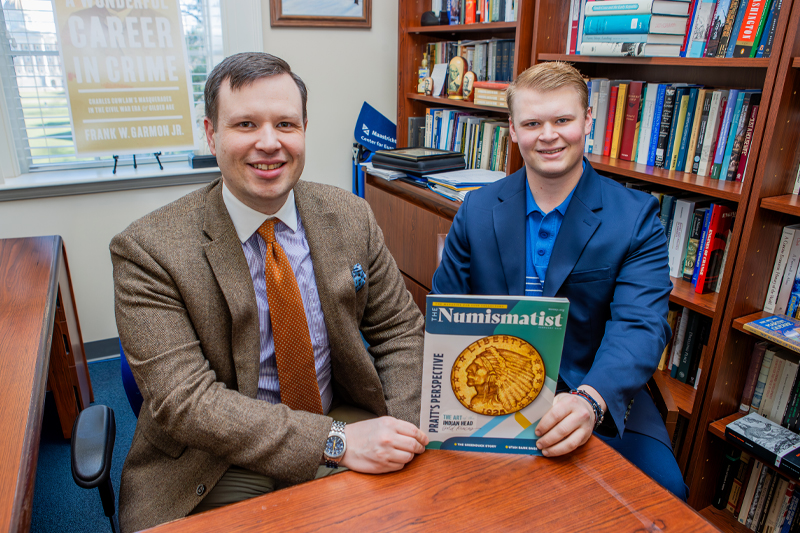 Frank Garmon and Dylan Frederick sit at a table holding the magazine that contains their research